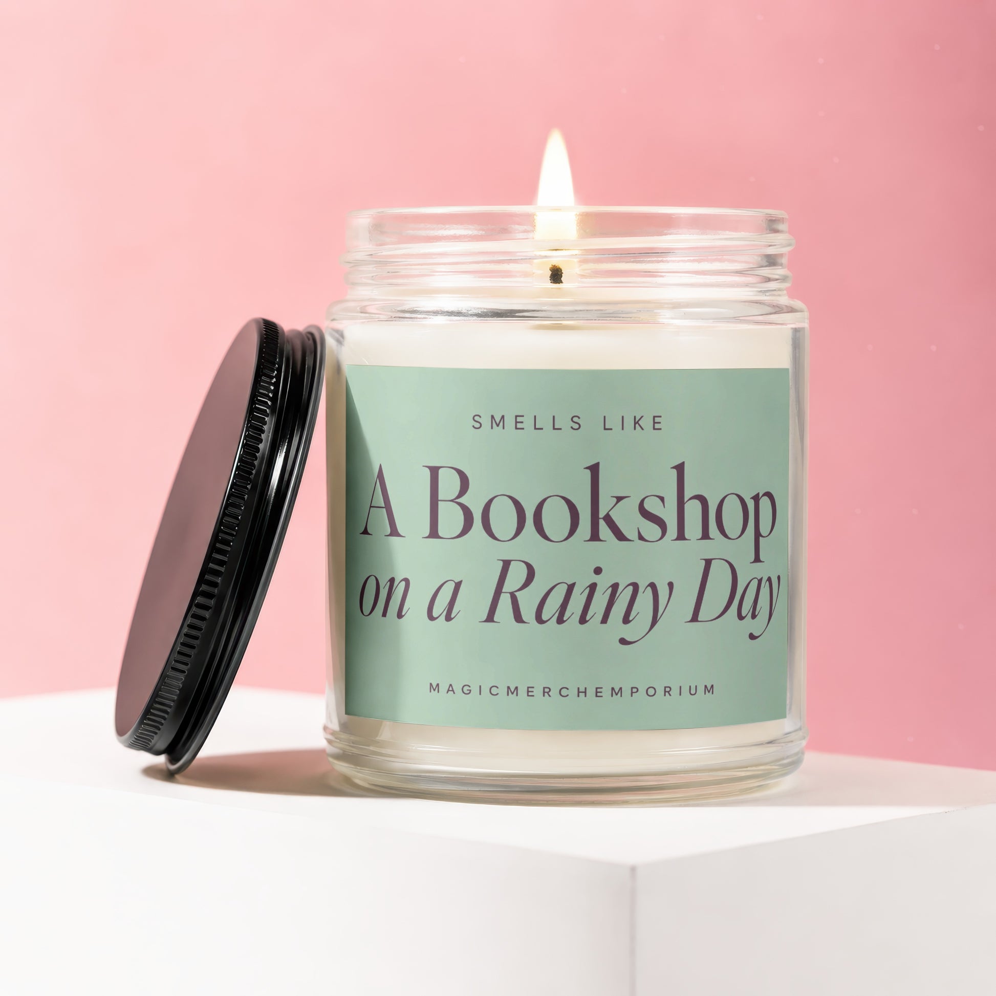 Glass jar candle with lid off, lit flame, "A Bookshop on a Rainy Day" text.