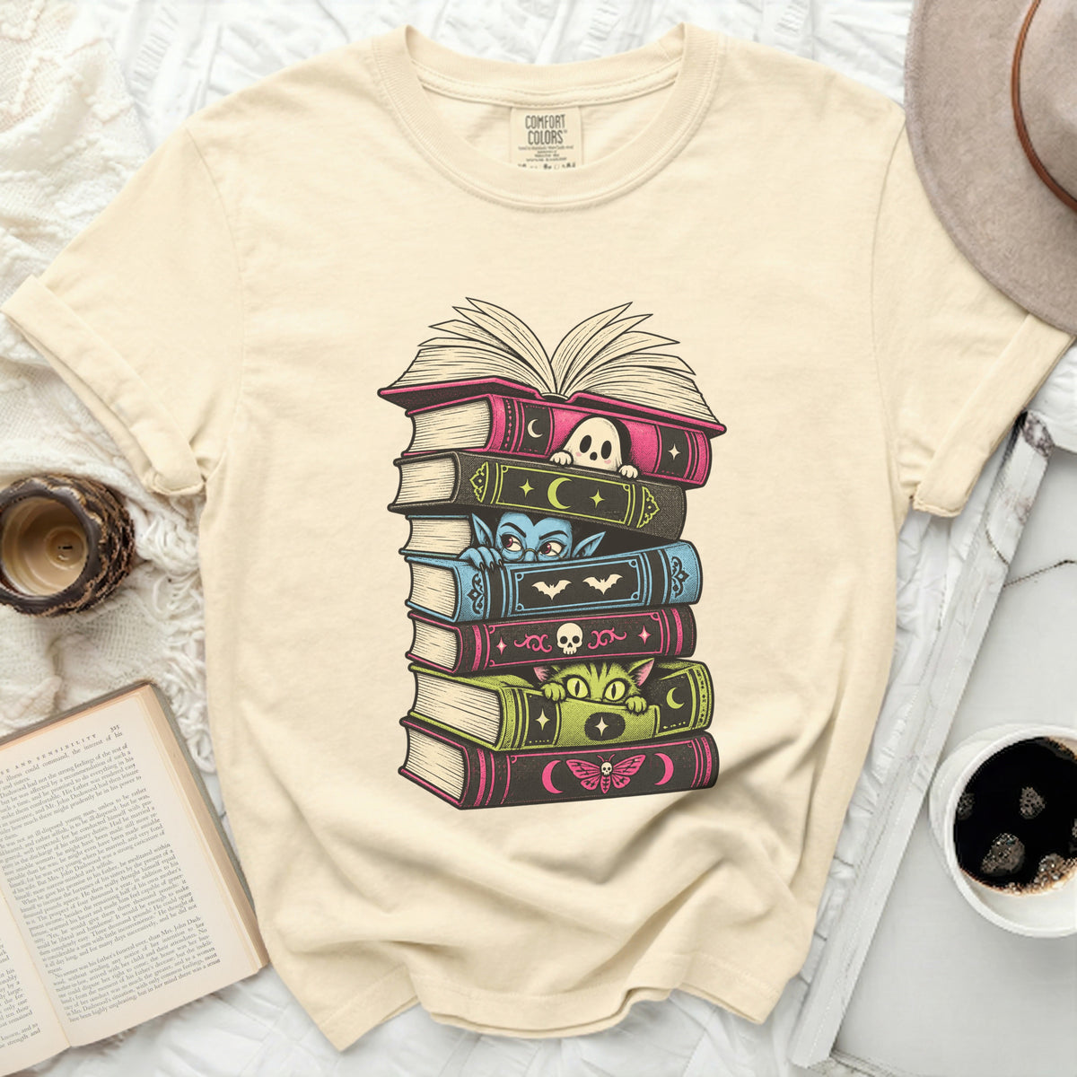 T-shirt with stacked books featuring a ghost, vampire, cat, and moth illustration.