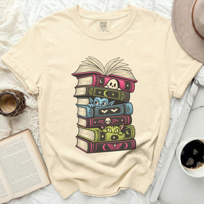 T-shirt with stacked books featuring a ghost, vampire, cat, and moth illustration.