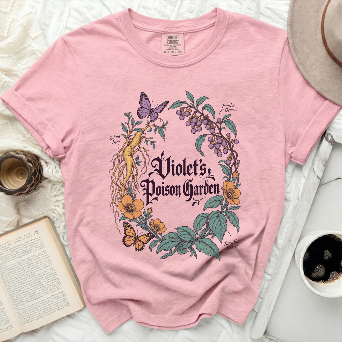 Pink t-shirt with a vintage botanical graphic featuring plants and the text Violet's Poison Garden.
