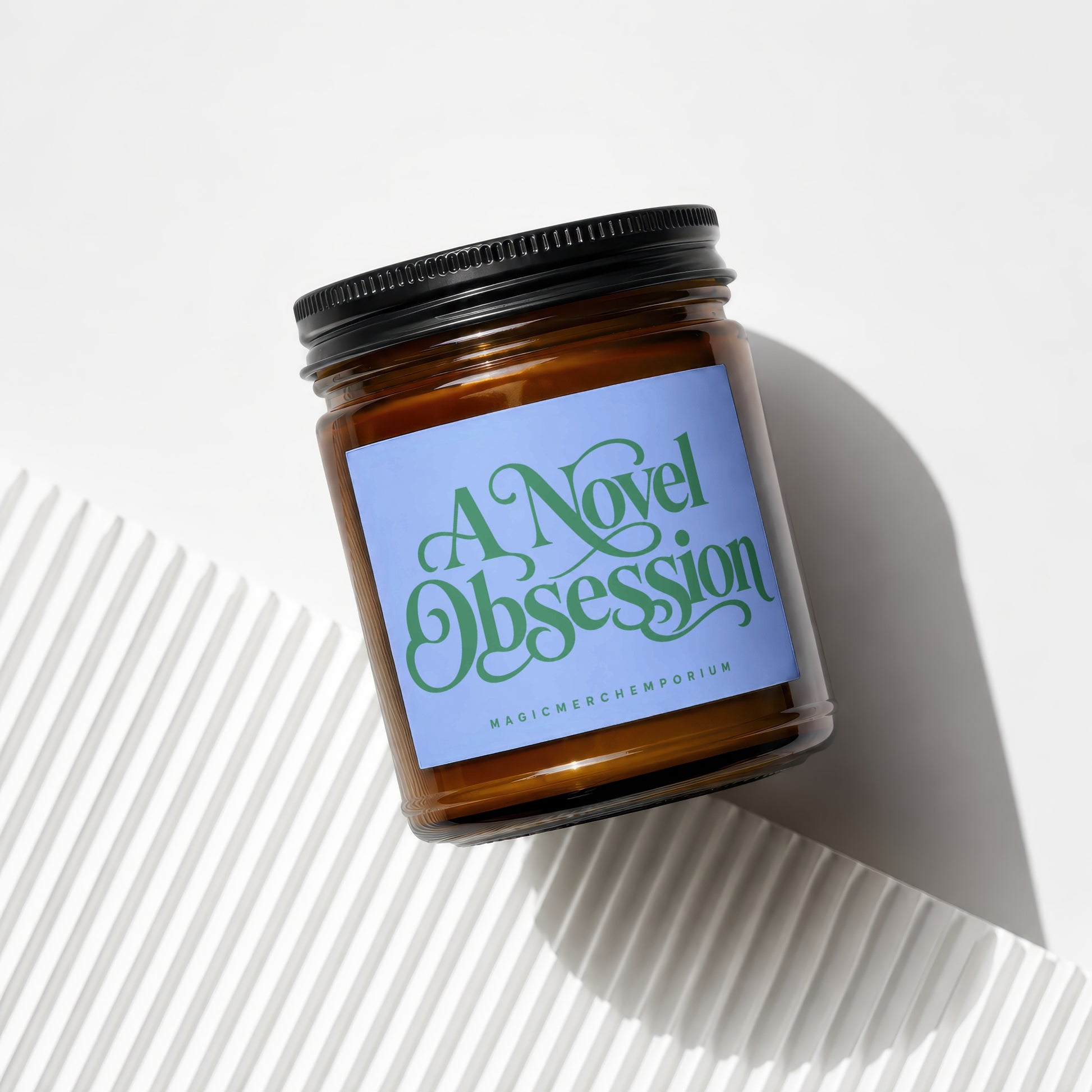 Brown glass candle with a blue label that reads "A Novel Obsession Magic Merch Emporium".