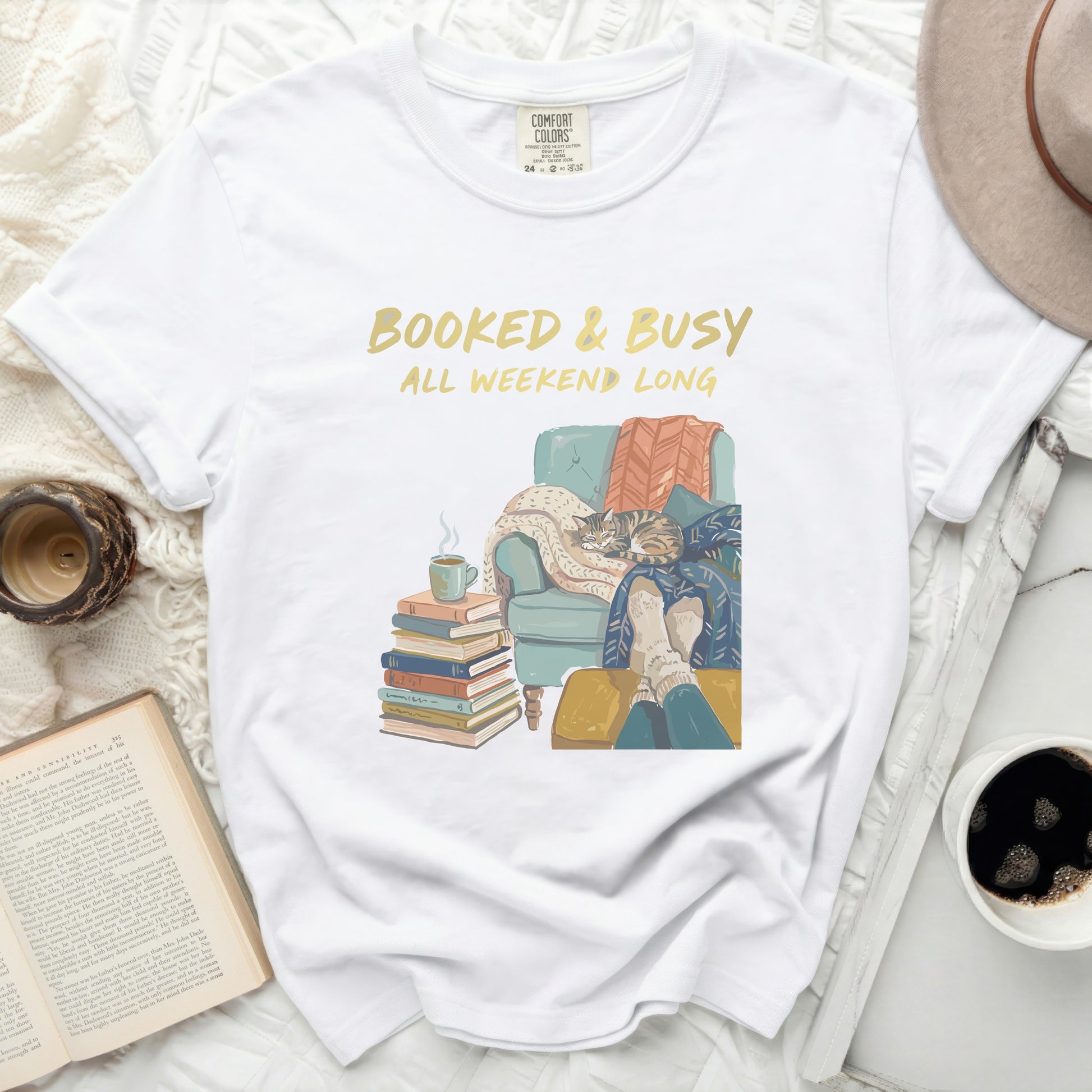 White t-shirt with "BOOKED & BUSY ALL WEEKEND LONG" text and cozy reading scene.