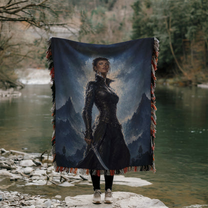 A woman stands in front of a large painting depicting a mountainous landscape, holding a large blanket or quilt with a painting of a woman on it.