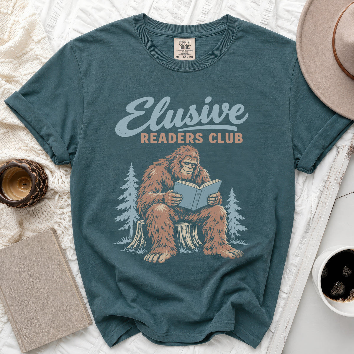 Teal t-shirt with Bigfoot reading a book, "Elusive Readers Club" text.