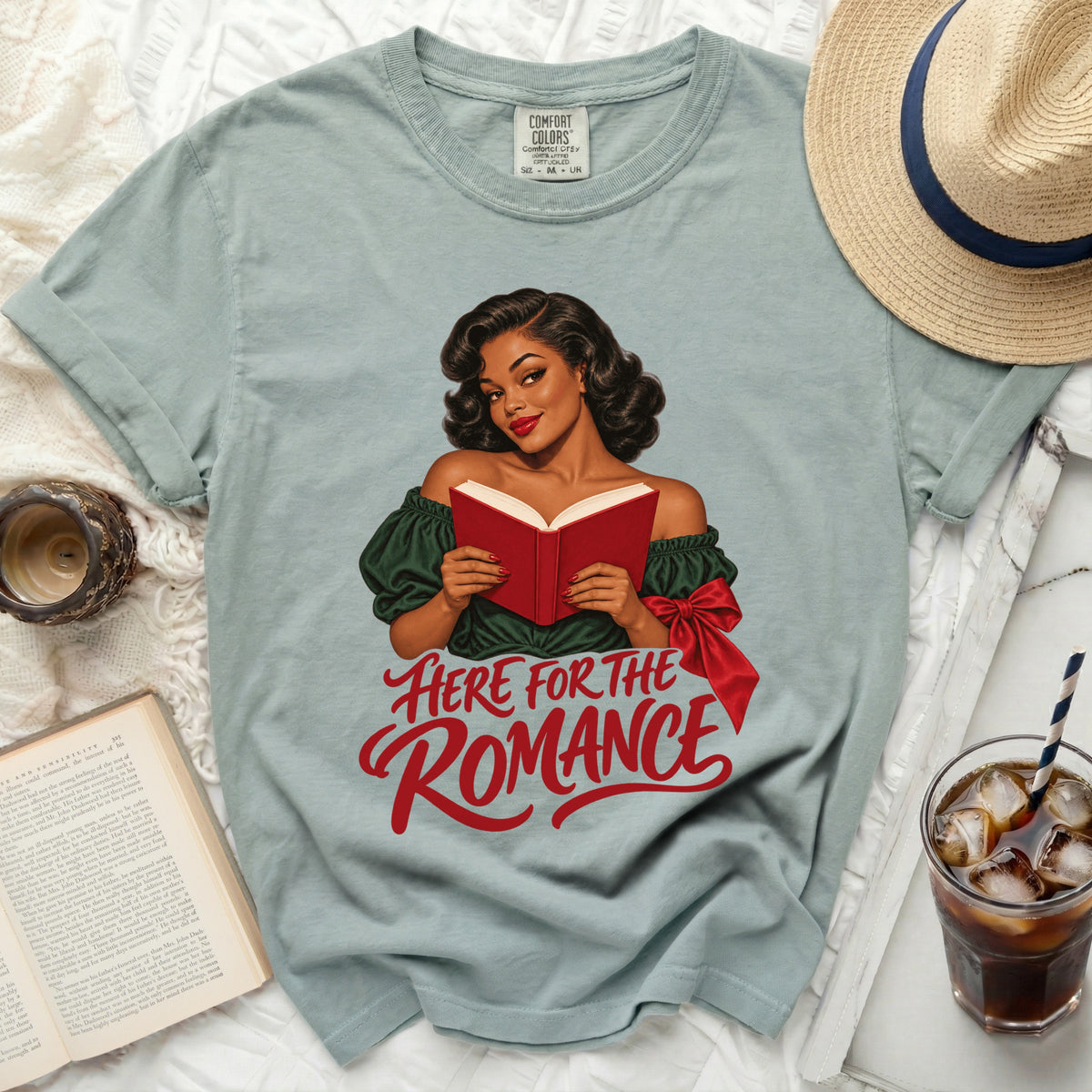 Light blue t-shirt with a graphic of a woman reading and text "HERE FOR THE ROMANCE".