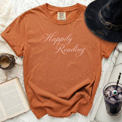 Orange t-shirt with "Happily Reading" in pink script, with witch hat and book.