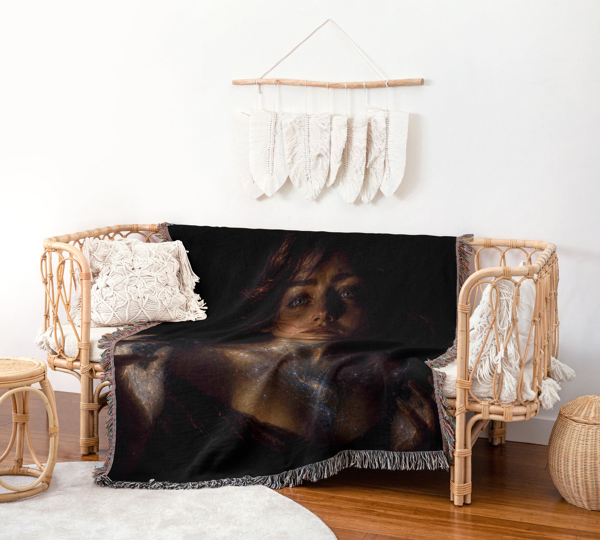 a cozy living space with a wicker chair, a woven basket, and a wall hanging with white feathers. The chair has a black blanket with a woman's face printed on it, and the wall hanging is hanging above the chair.