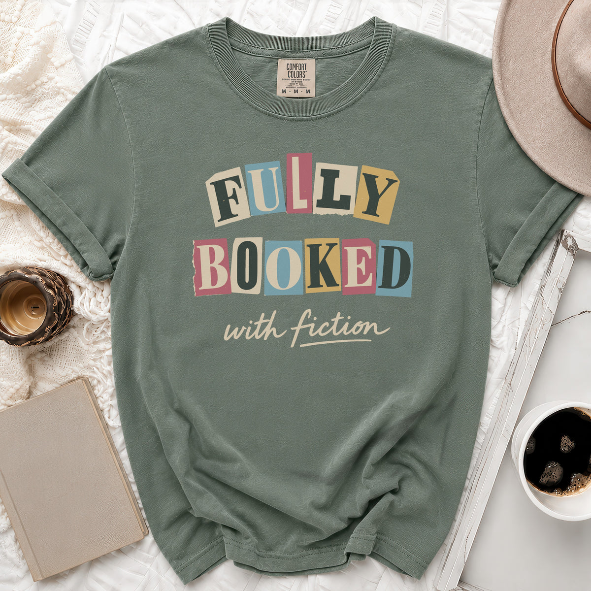 Sage green t-shirt with "Fully Booked with Fiction" text in colorful letters.