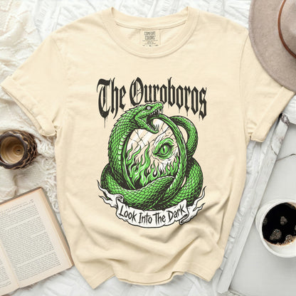 Cream t-shirt with a green Ouroboros snake design and text "The Ouroboros Look Into The Dark".