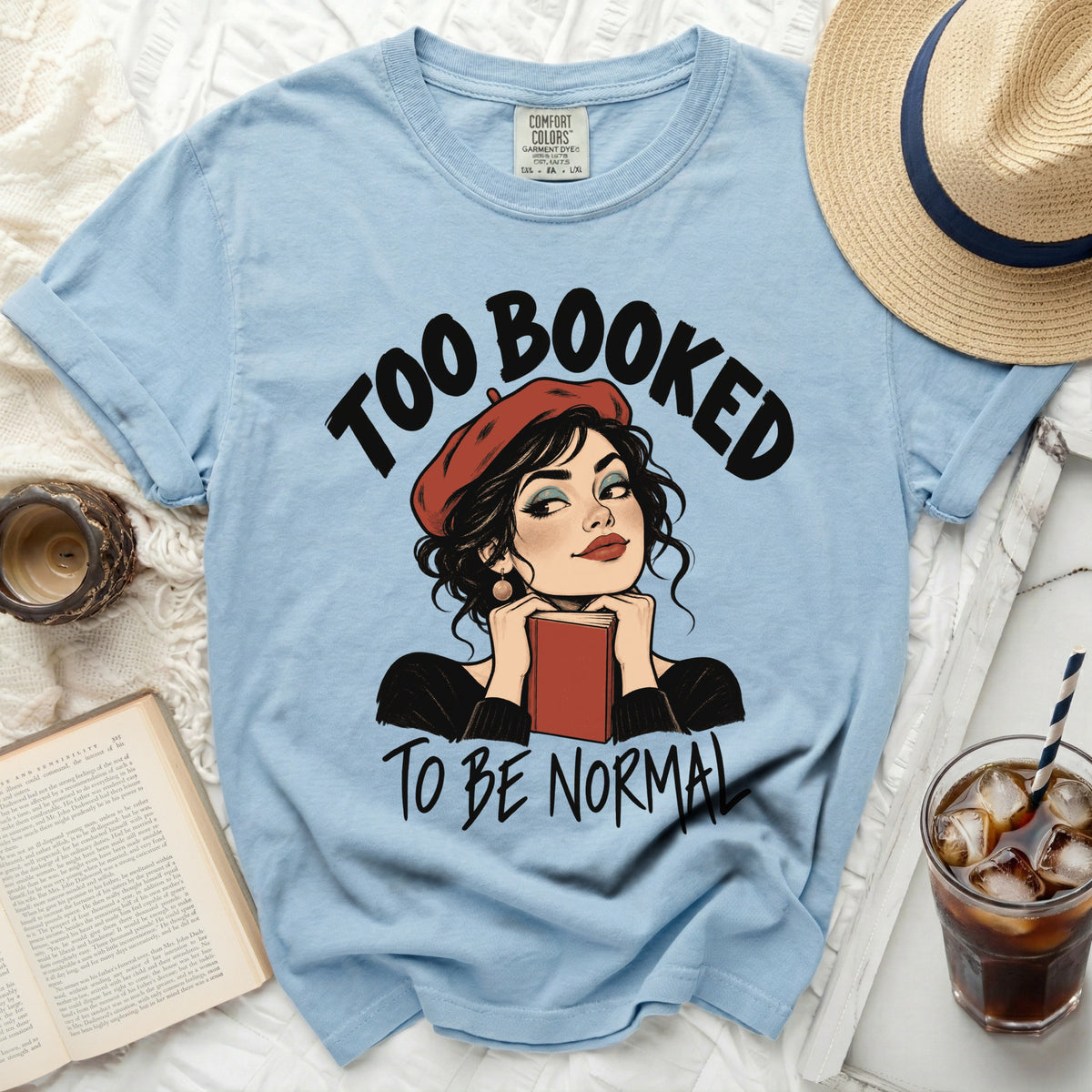 Light blue t-shirt with "Too Booked To Be Normal" graphic and woman holding a book.