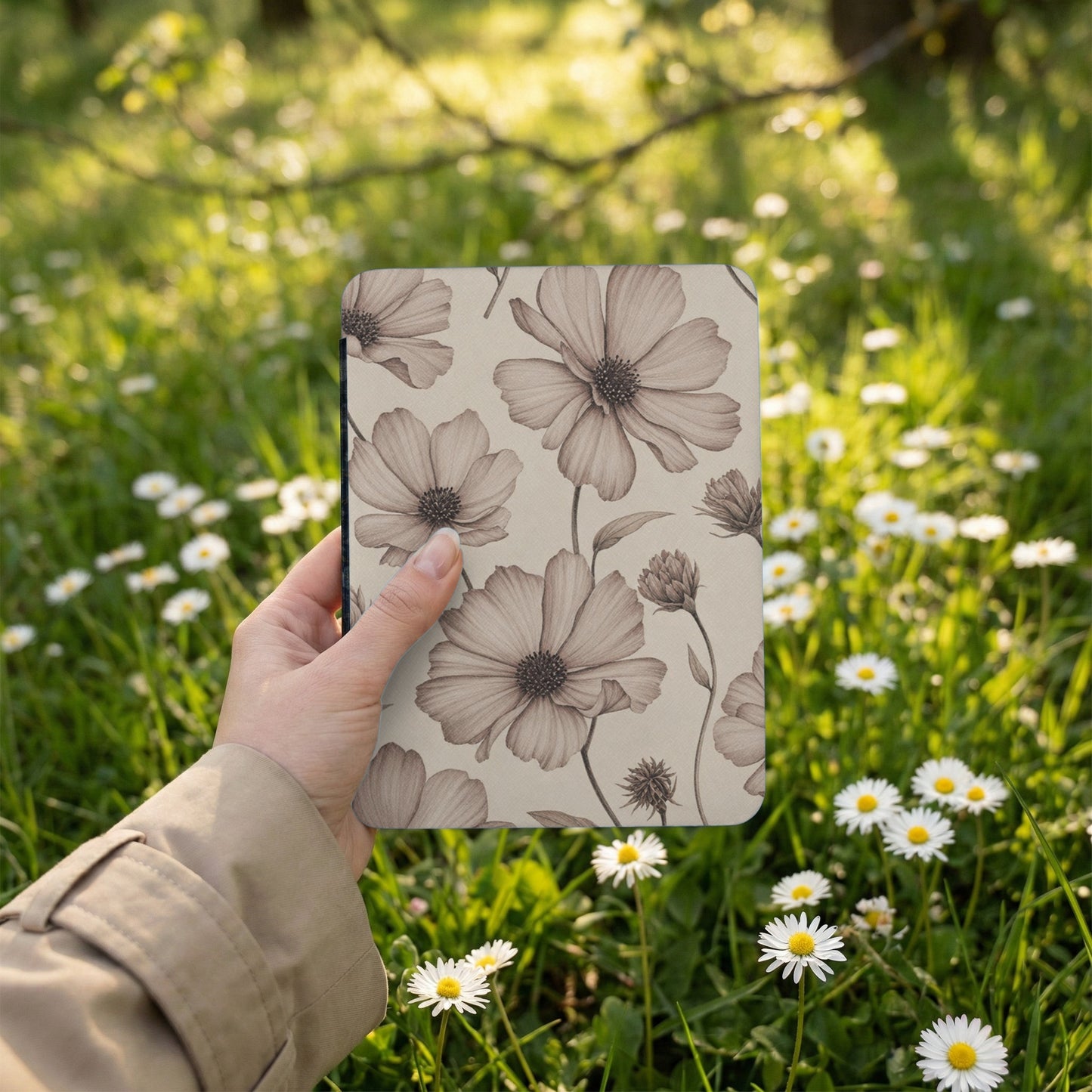 Hand holds a journal with a sepia floral pattern against a background of daisies.