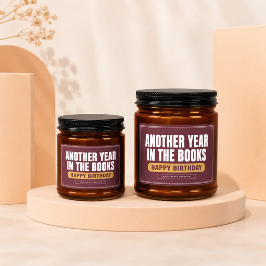 Two amber glass candles with black lids, labeled "Another Year In The Books Happy Birthday".