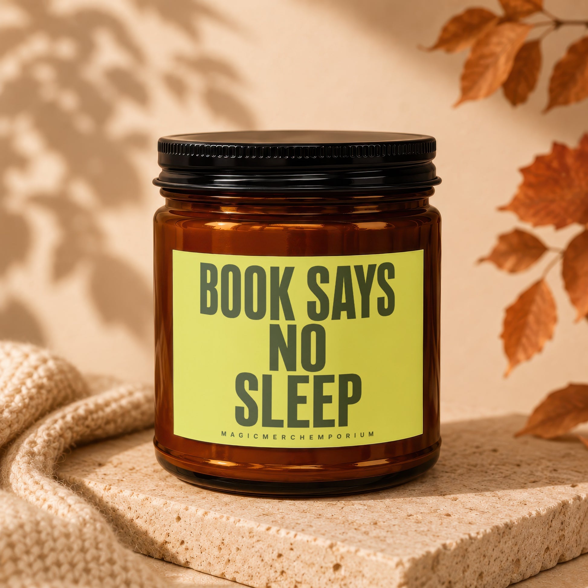 Amber jar candle with black lid; yellow label reads "BOOK SAYS NO SLEEP MAGIC MERCH EMPORIUM".