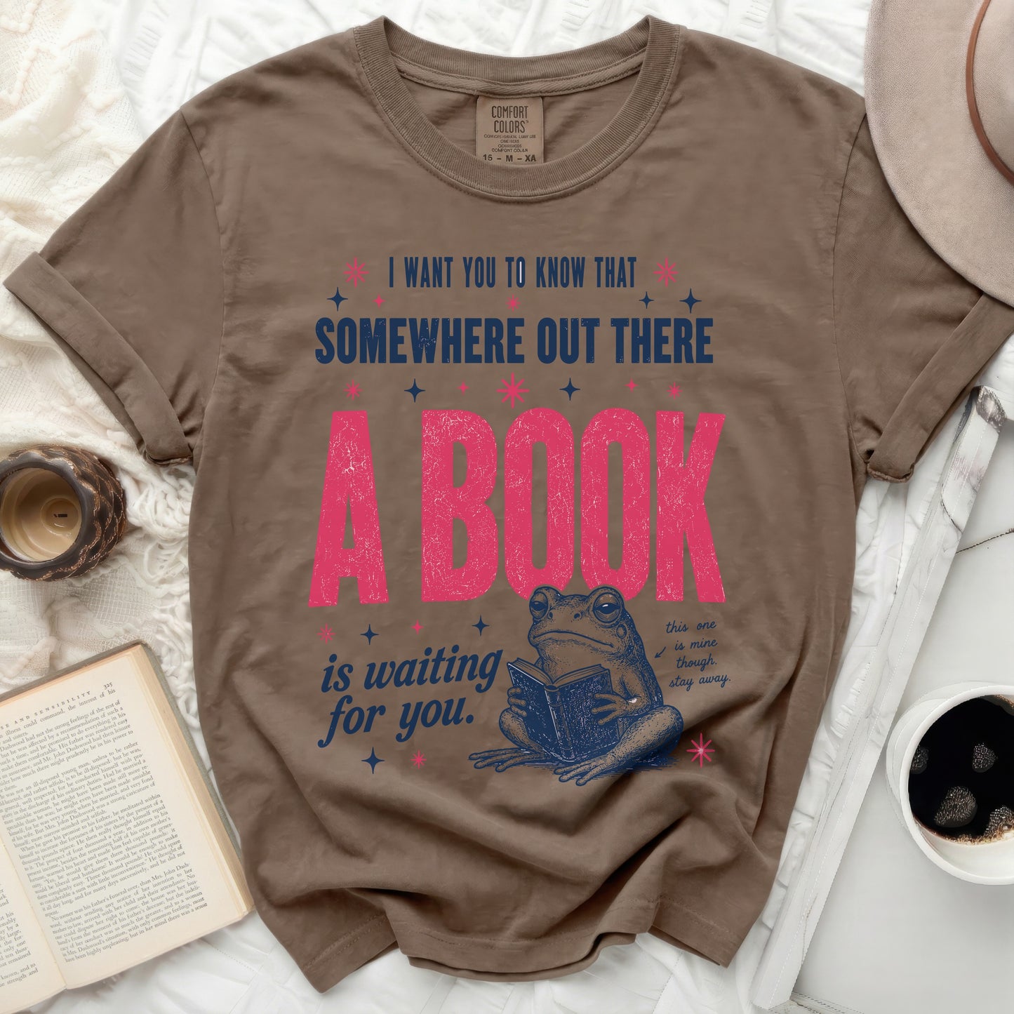Brown t-shirt with pink text and a frog reading a book.