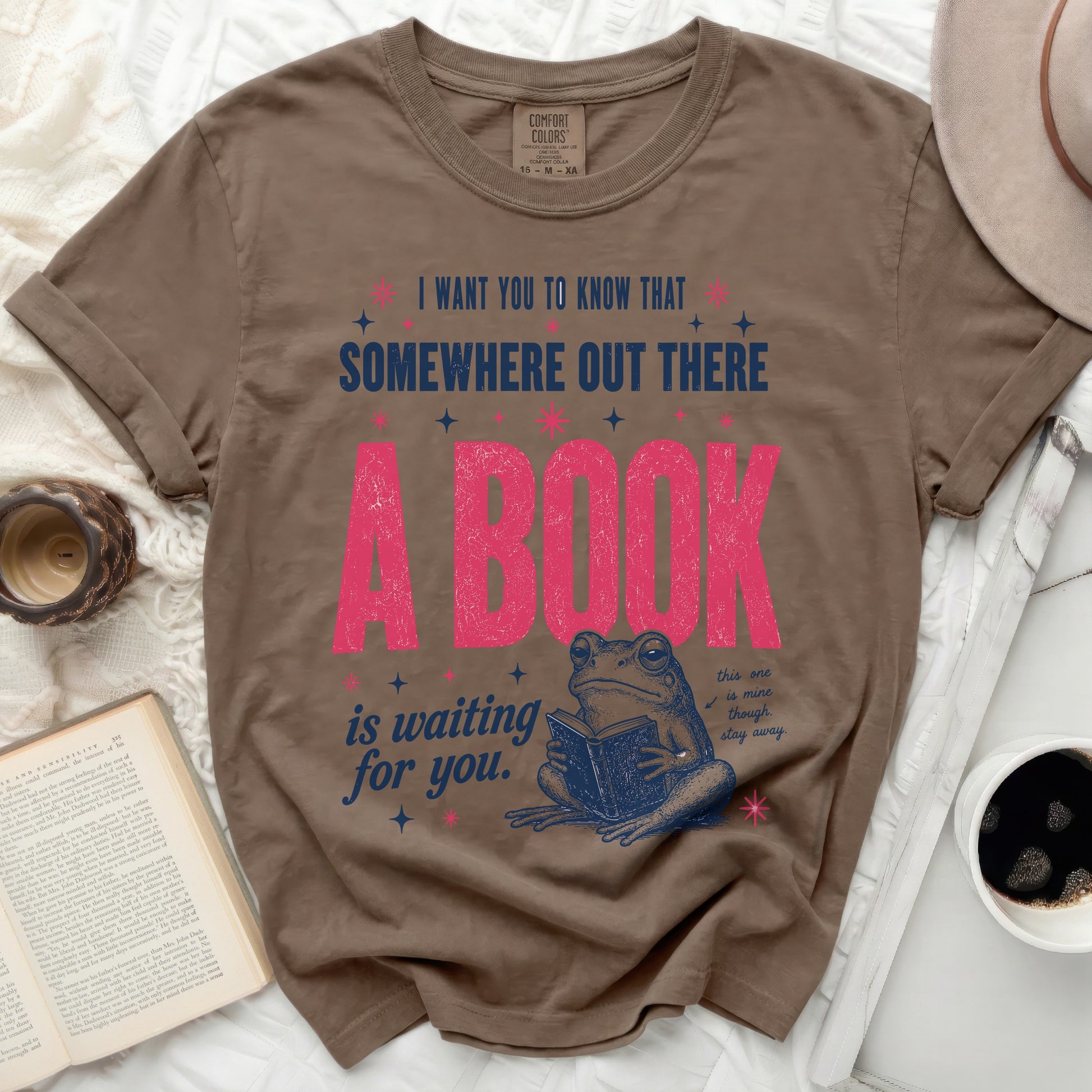 Brown t-shirt with pink text and a frog reading a book.