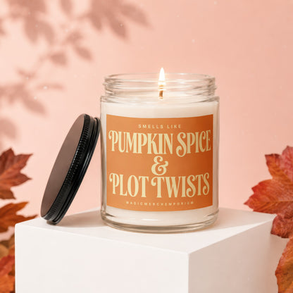 Glass jar candle with orange label reading "Smells Like Pumpkin Spice & Plot Twists"