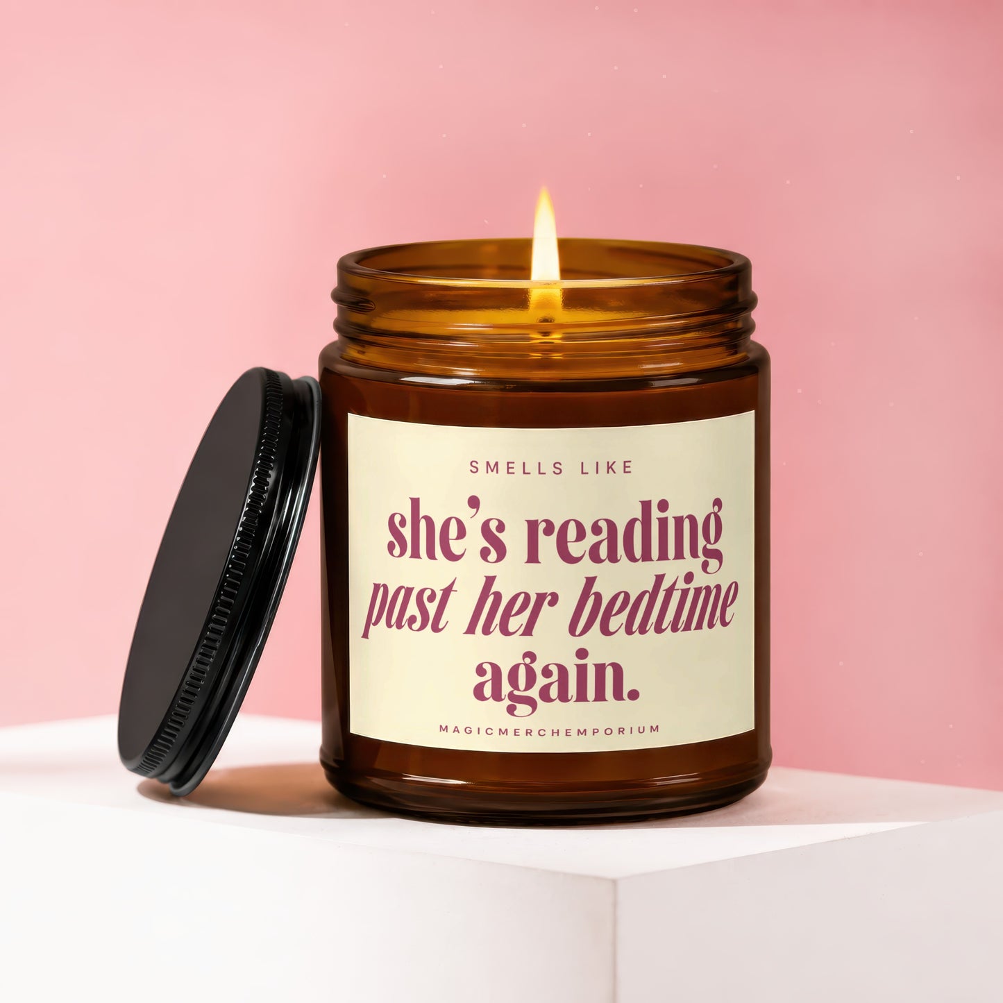 Amber candle with lit wick, reading "Smells like she's reading past her bedtime again."