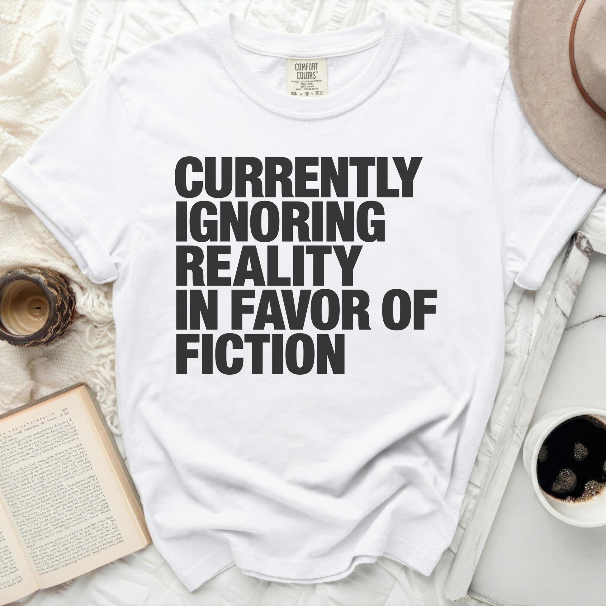 White t-shirt with black text reading "Currently Ignoring Reality in Favor of Fiction".