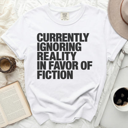 White t-shirt with black text reading "Currently Ignoring Reality in Favor of Fiction".
