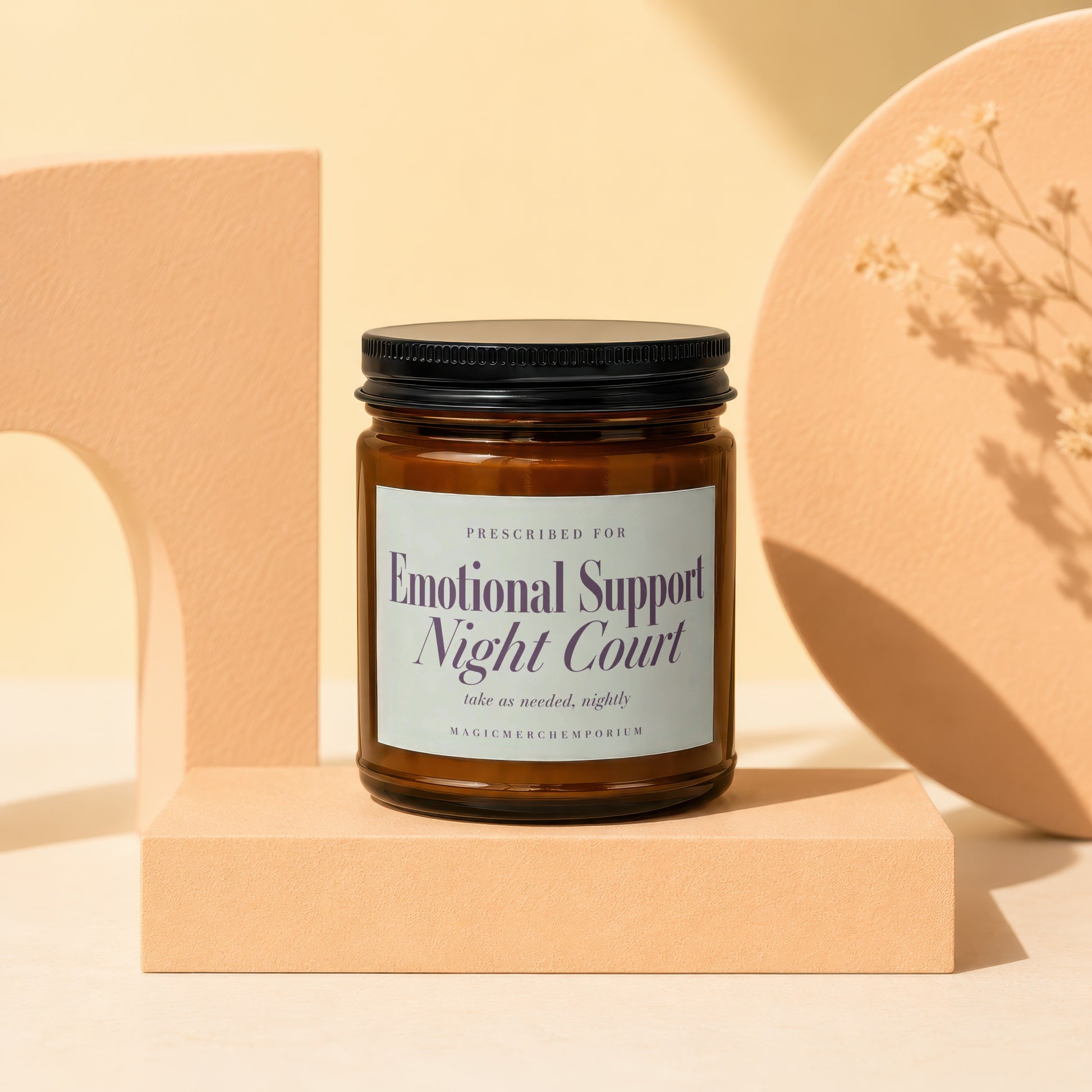 Amber glass candle with "Emotional Support Night Court" label on beige pedestal.