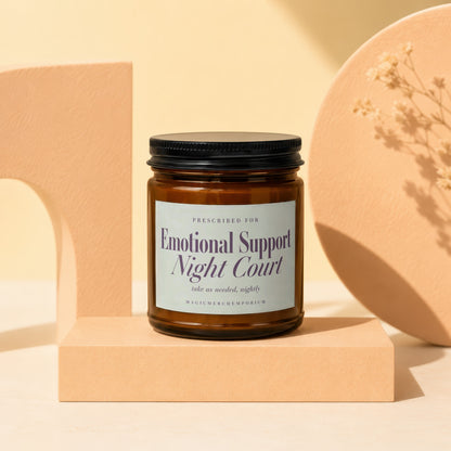 Amber glass candle with "Emotional Support Night Court" label on beige pedestal.