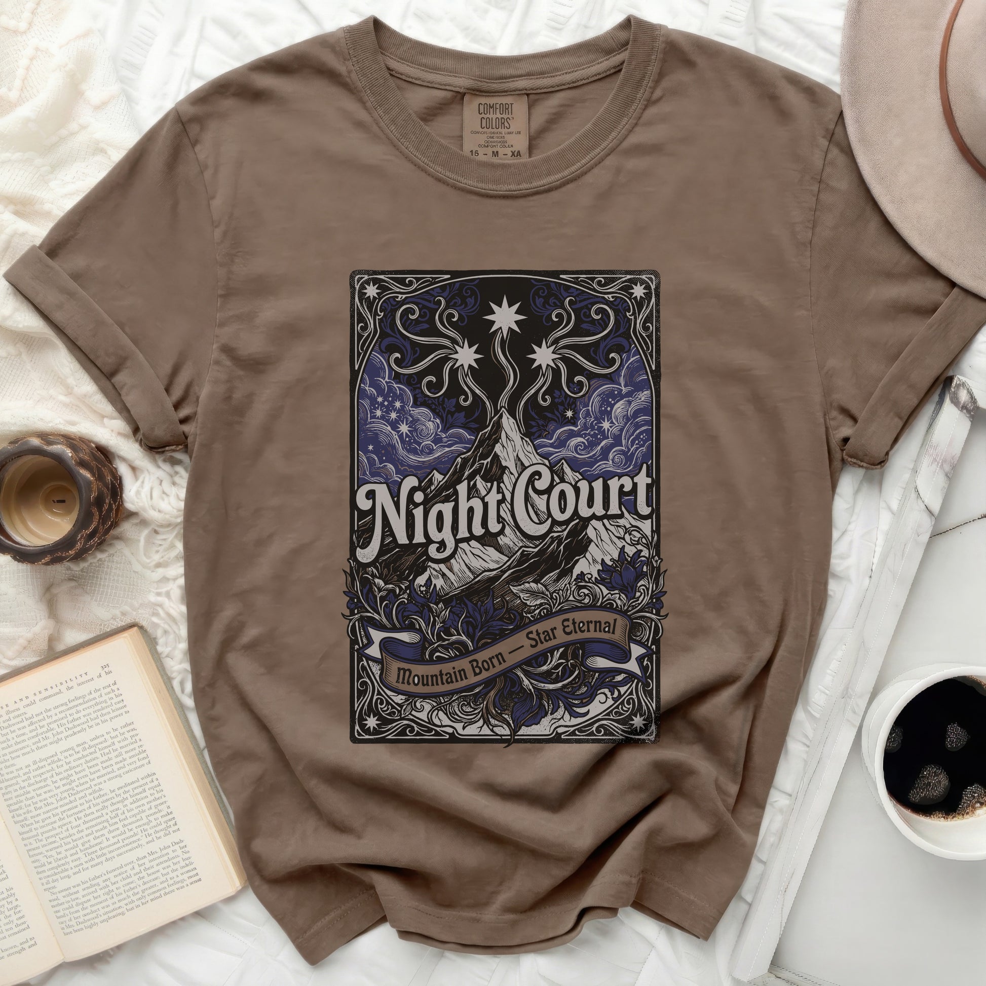 Brown t-shirt with "Night Court Mountain Born Star Eternal" text and celestial design.