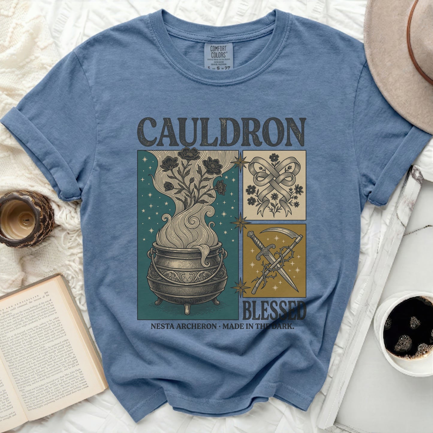 Blue t-shirt with a four-panel graphic featuring a cauldron, flowers, ribbon, and scythe with text.