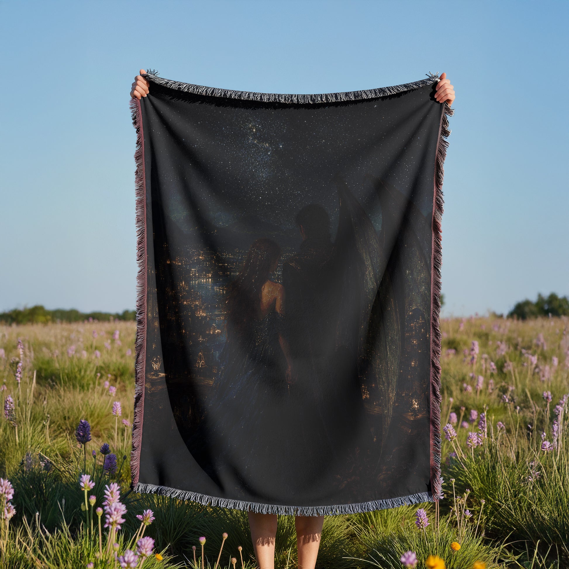 A person is holding a black blanket with a printed image of two people on it, standing in a field of purple flowers.