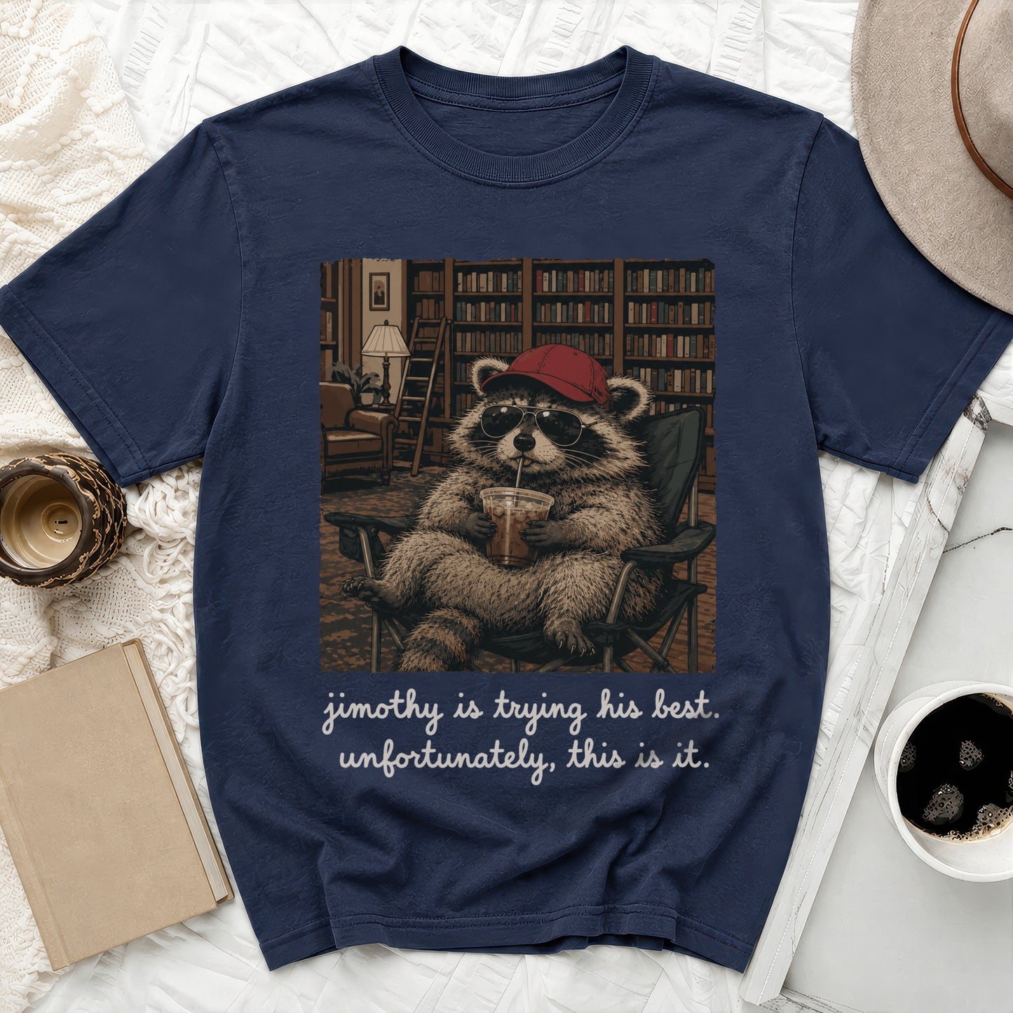T-shirt graphic of a raccoon wearing sunglasses and a hat, drinking from a cup, with text.