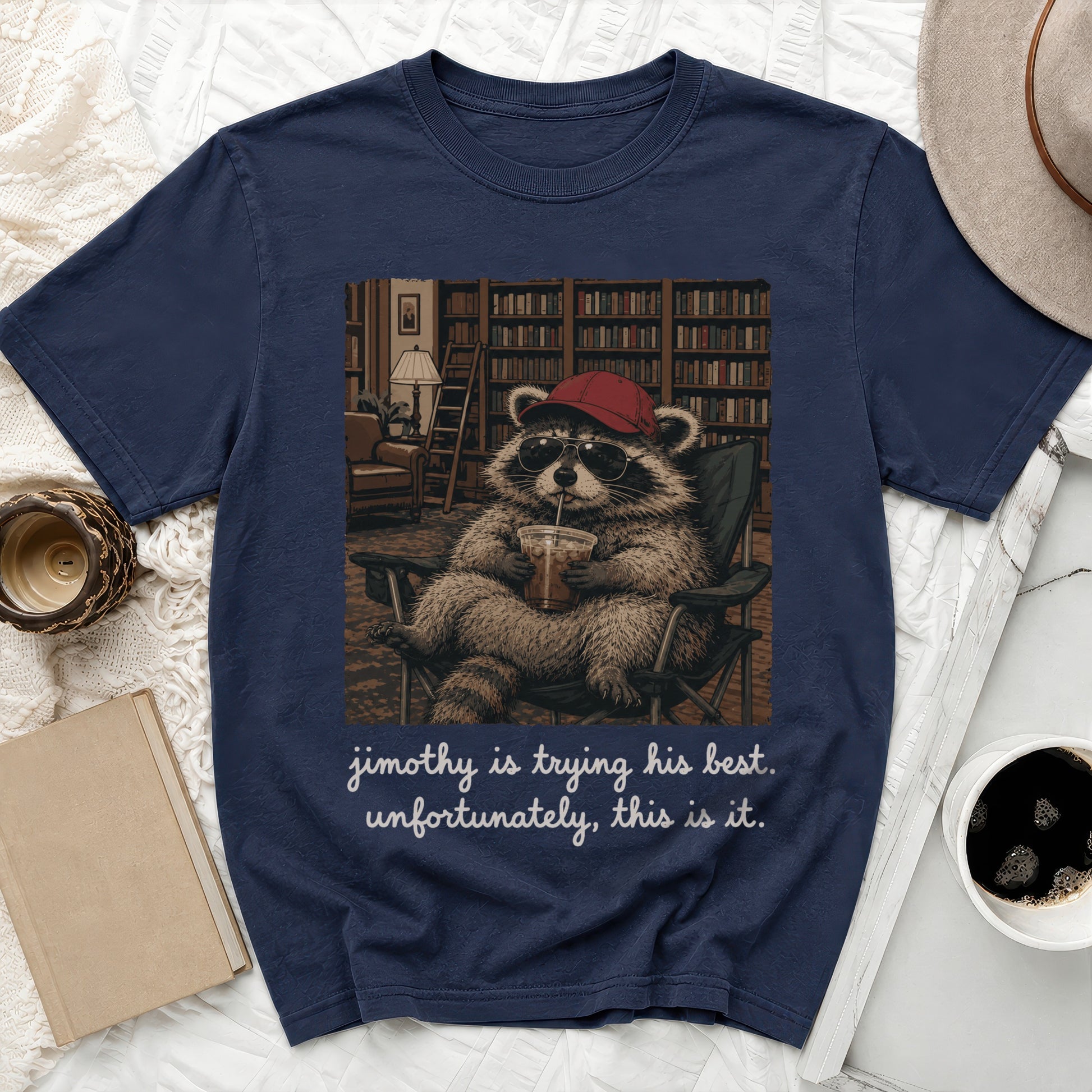 T-shirt graphic of a raccoon wearing sunglasses and a hat, drinking from a cup, with text.