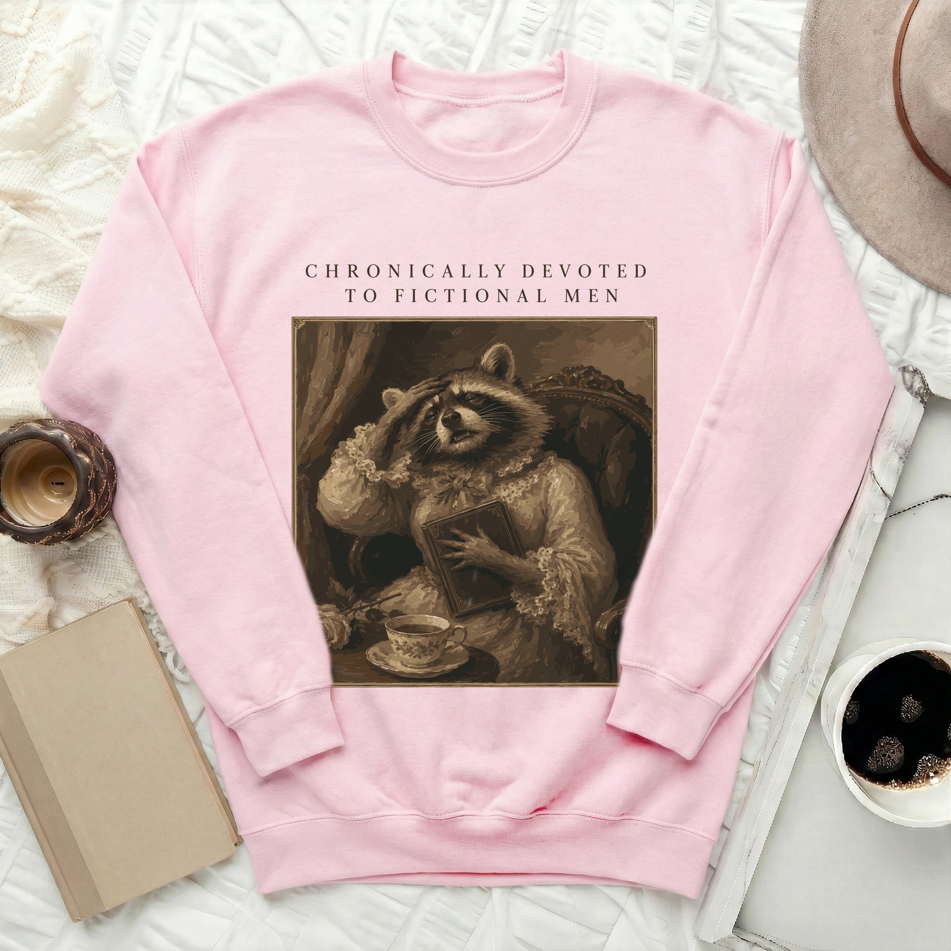 Pink sweatshirt with "CHRONICALLY DEVOTED TO FICTIONAL MEN" text and raccoon illustration.