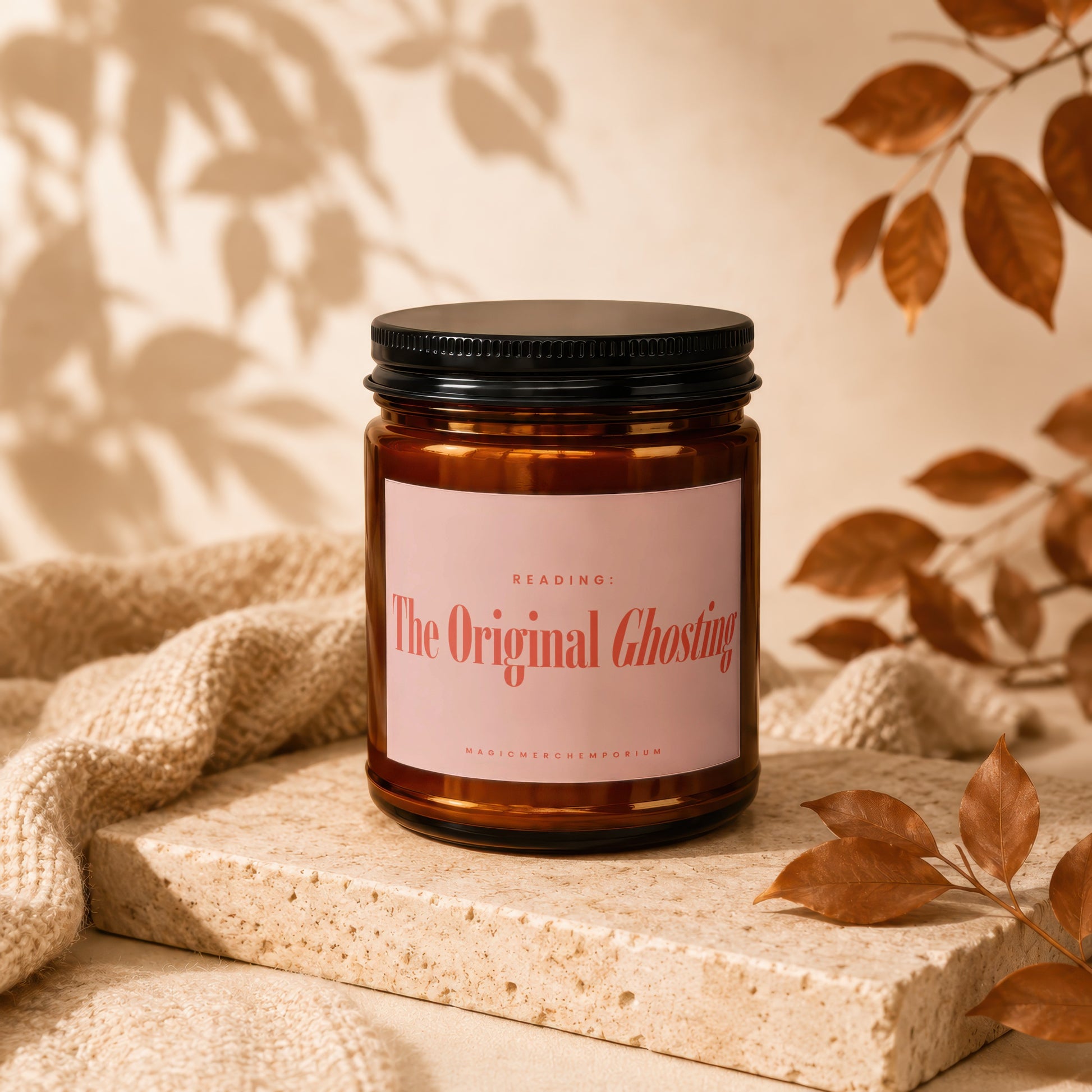 Amber candle with label reading "The Original Ghosting," on textured stone with autumn leaves.