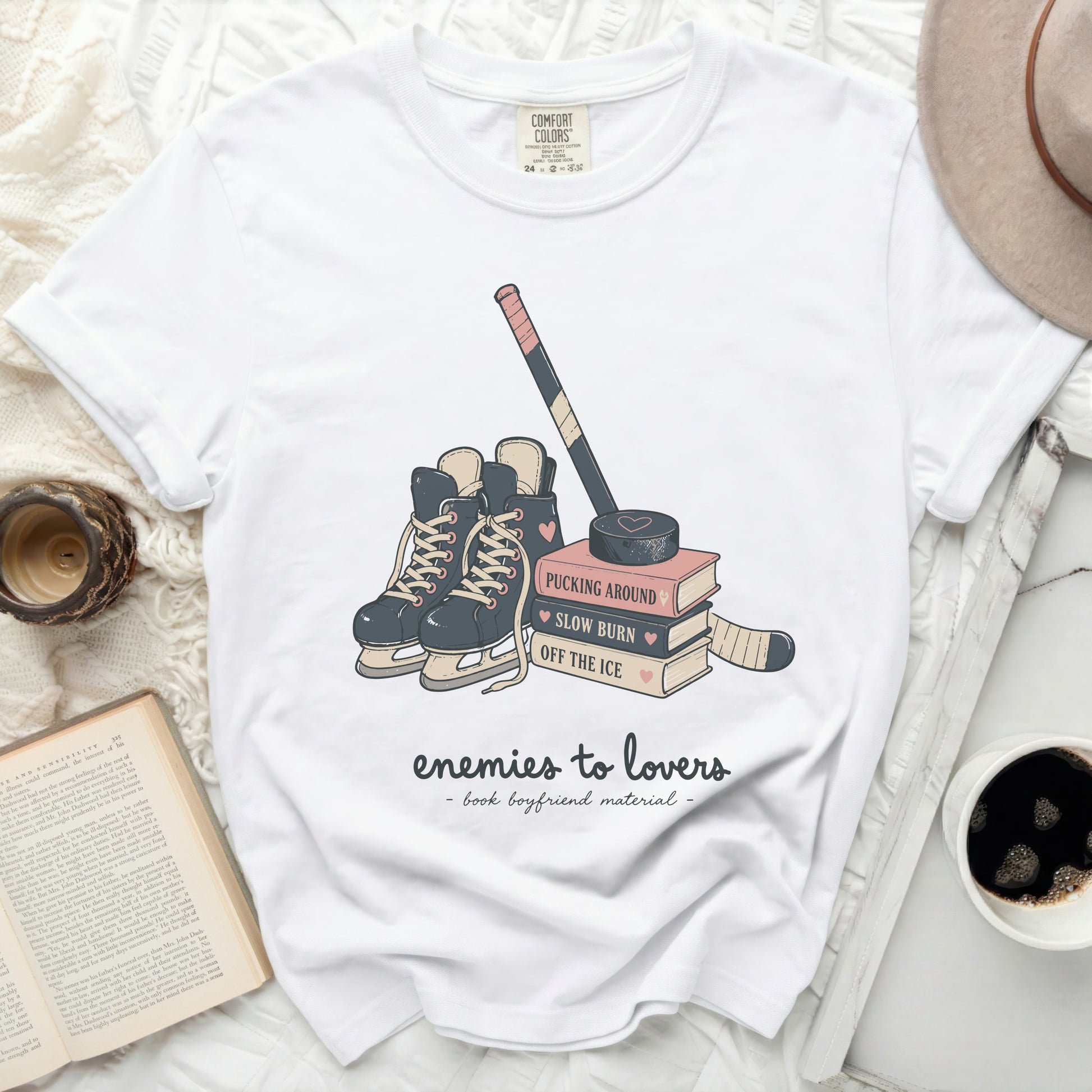 White t-shirt with hockey skates, stick, and books graphic, text "enemies to lovers".