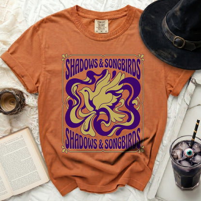 Orange t-shirt with "Shadows & Songbirds" text and a stylized bird design.