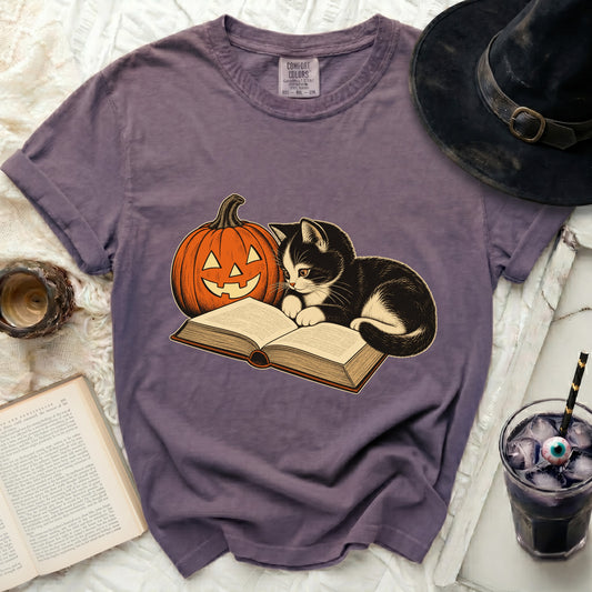 T-shirt with black and white kitten reading next to a jack-o'-lantern.