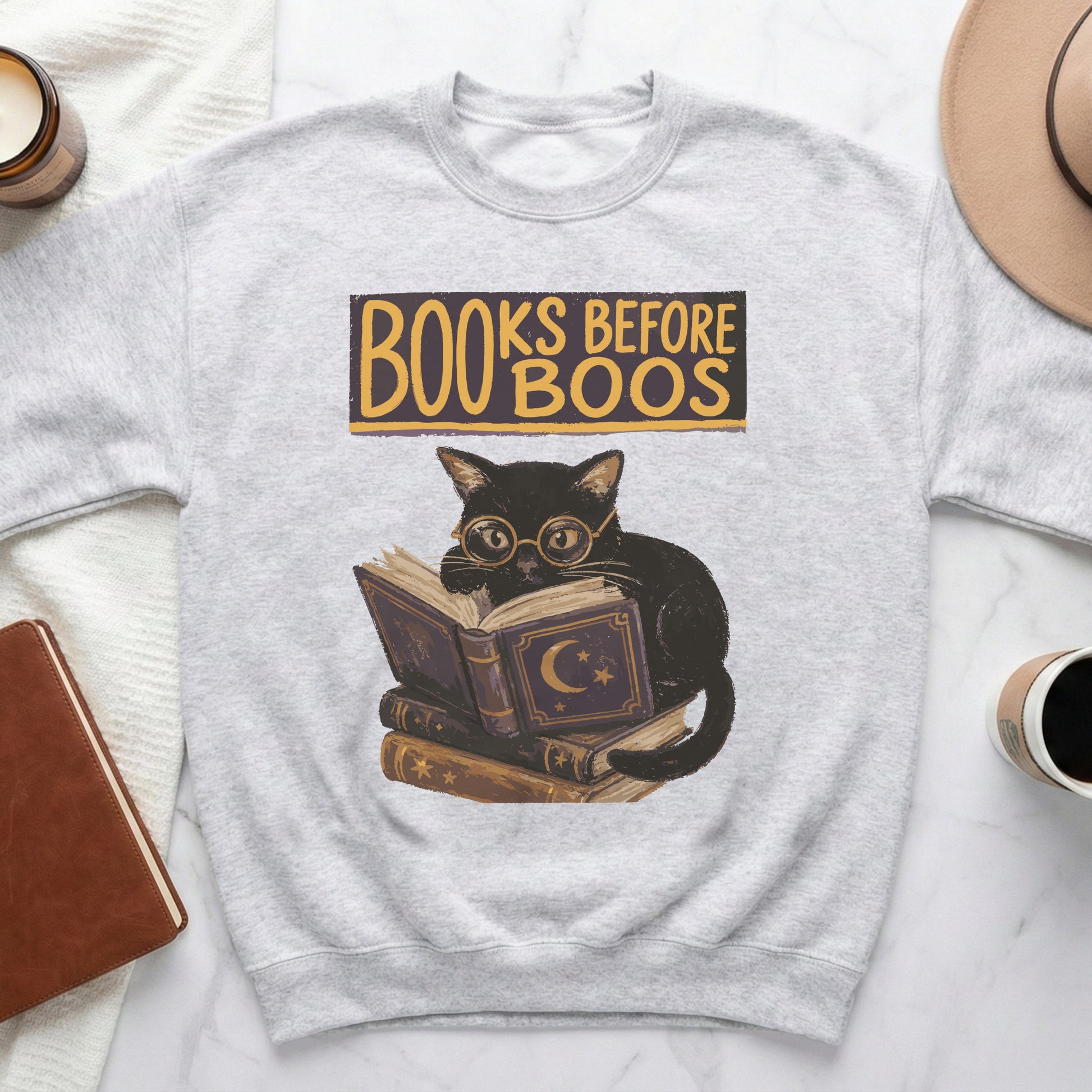 Grey sweatshirt with a cat wearing glasses reading books, text "Books Before Boos".