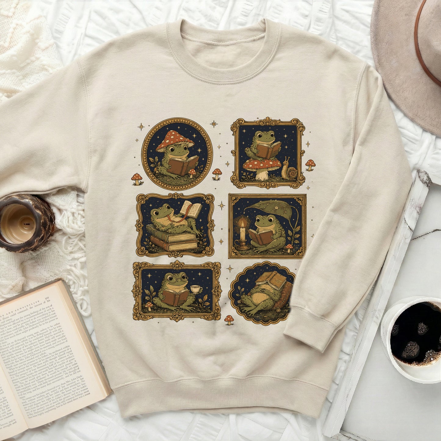 Six illustrated frogs reading books among mushrooms and stars on a cream sweatshirt.