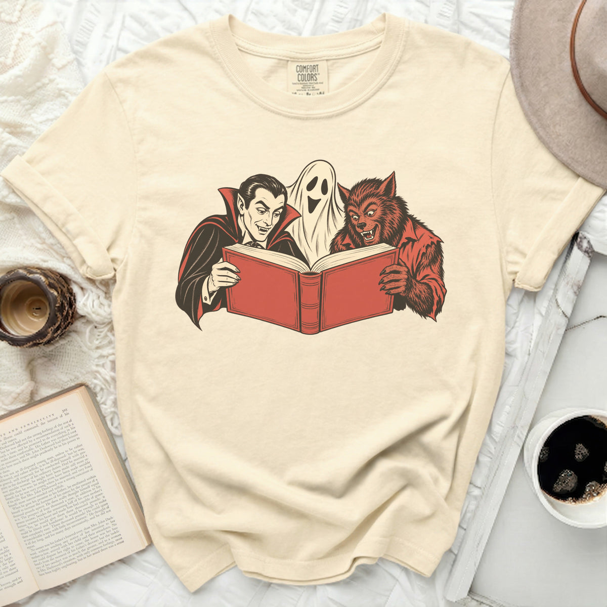 Vampire, ghost, and werewolf reading a book on a cream t-shirt.