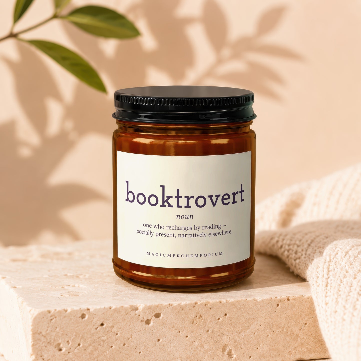 Amber jar candle with "booktrovert" definition label and black lid, on stone.