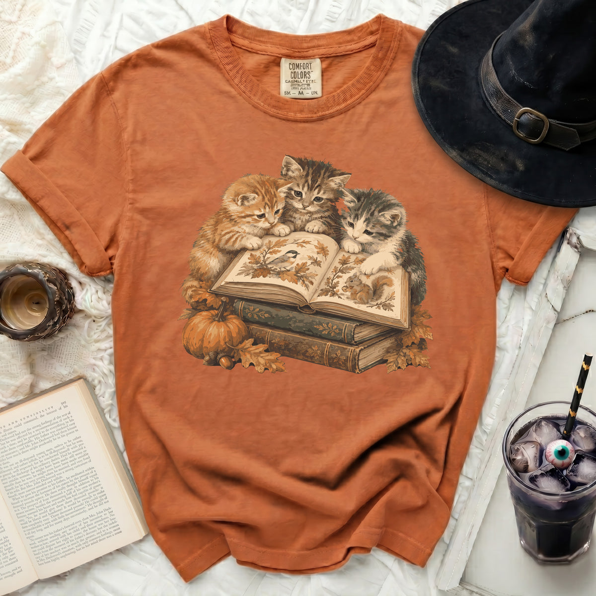 Three kittens read a book with autumn leaves and a pumpkin.