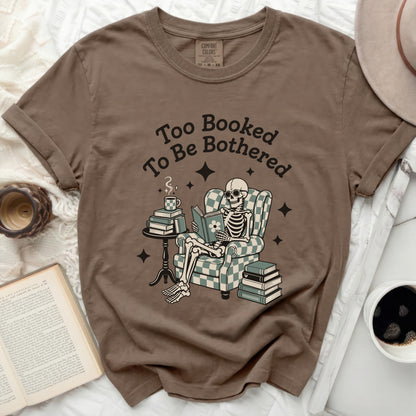 Brown t-shirt with graphic of skeleton reading with books and coffee.