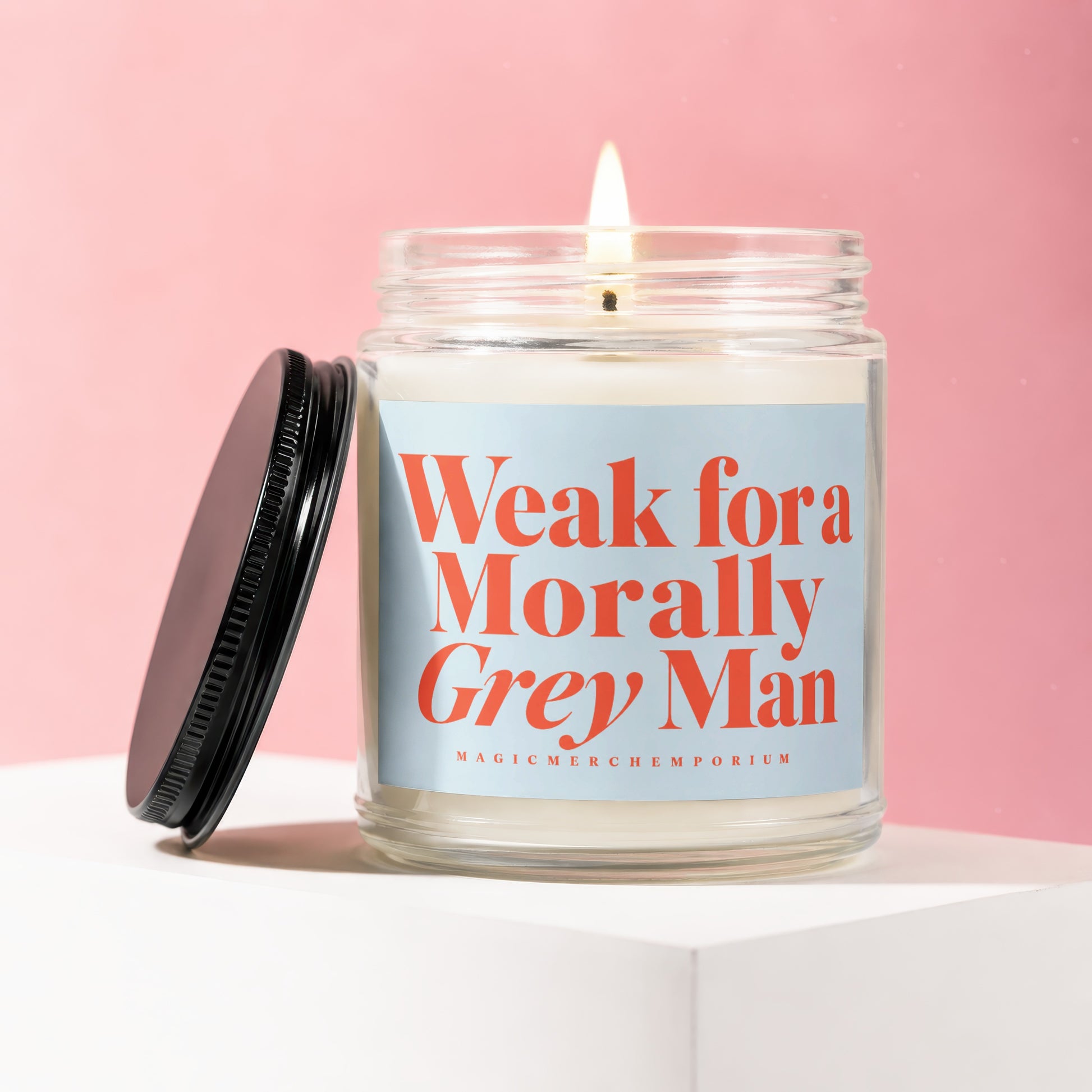 Glass candle with lit flame and label reading "Weak fora Morally Grey Man".