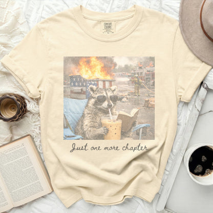 Cream t-shirt with raccoon reading book, text "Just one more chapter."