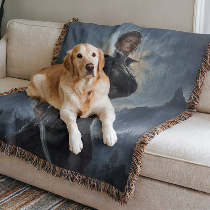 A golden retriever dog is lying on a blue and black blanket with a painting of a woman on it, placed on a white couch.