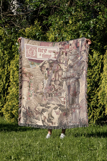 A person is holding up a large blanket with a medieval-style illustration on it, which includes a knight, castle, and other fantastical elements.