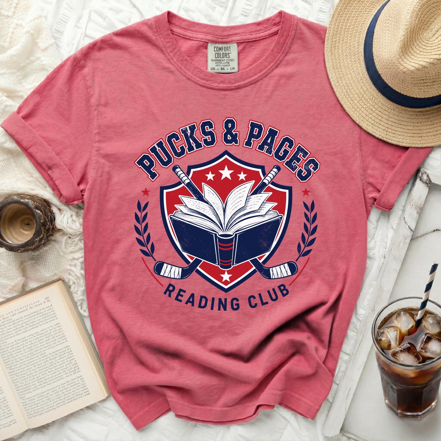 T-shirt with "Pucks & Pages Reading Club" logo and hockey sticks.