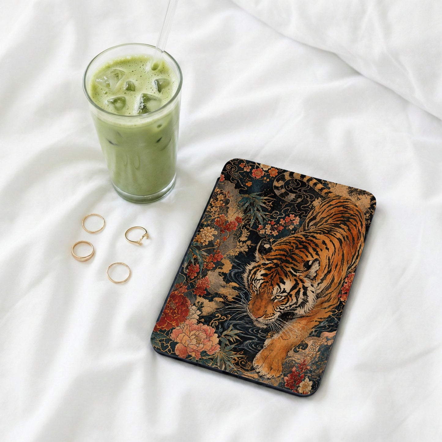 Phone case with tiger, flowers, and rings next to a matcha drink.