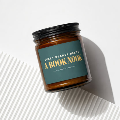 Amber jar candle with dark green label reading "Every Reader Needs A Book Nook Magic Merch Emporium".