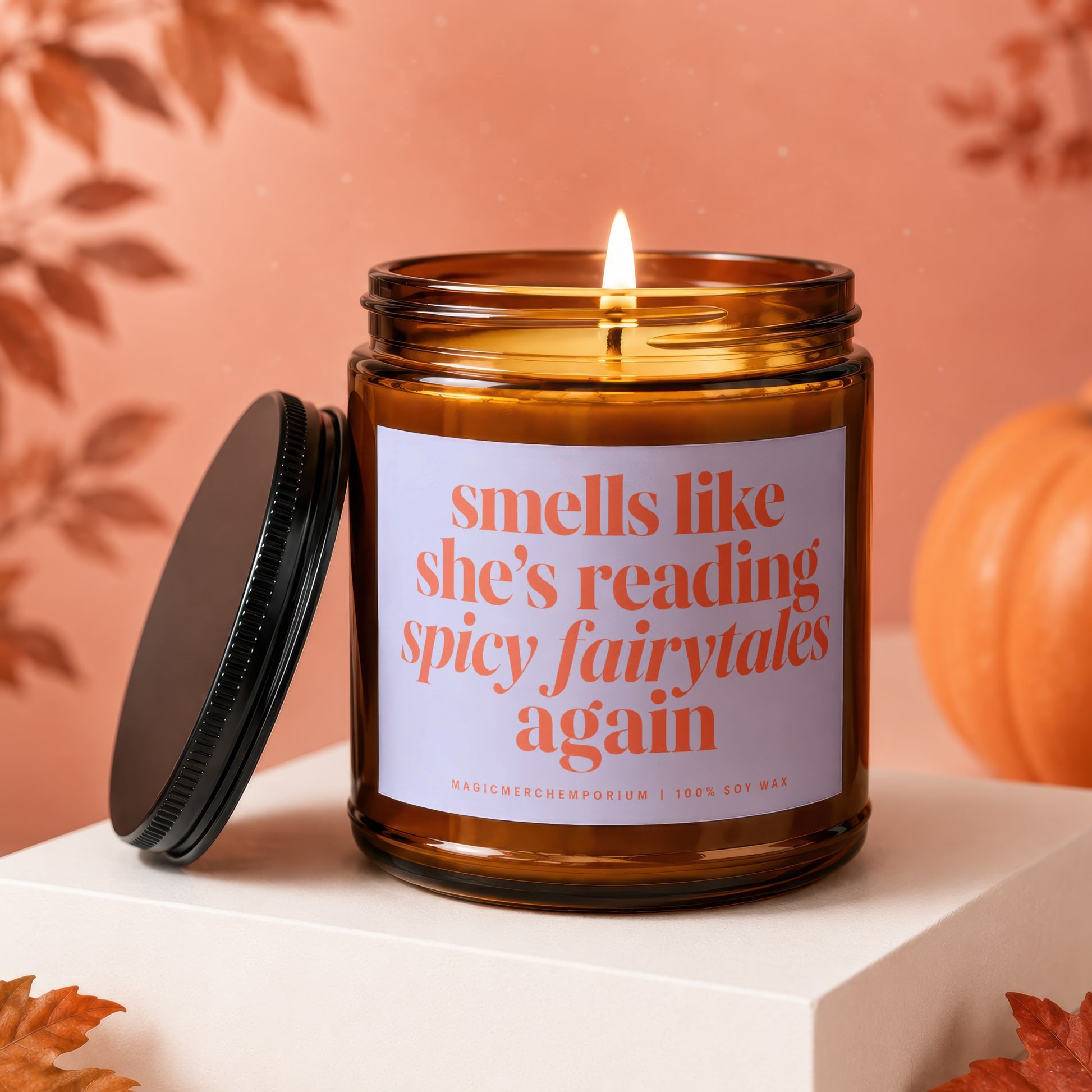 Amber glass candle with a lit wick and a black lid, reads "smells like she's reading spicy fairytales again".