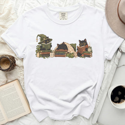 White t-shirt with print of three black cats reading books and witch hats.